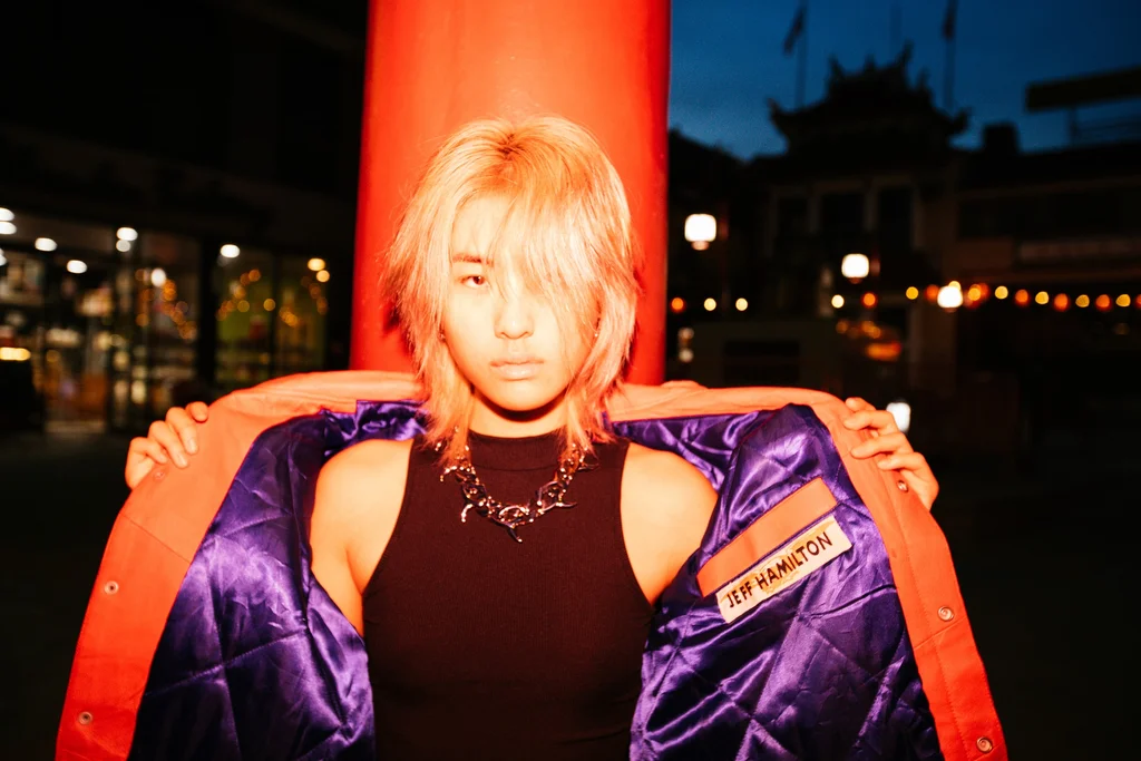 A flash-lit portrait in a purple jacket against a red pillar at night